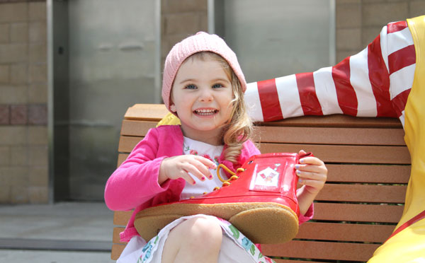 Little girl sitting with Ronald McDonald statue with a big smile on her face